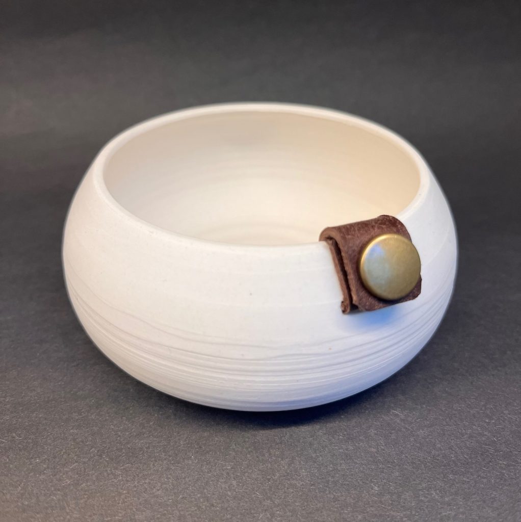 Small porcelain vessel with leather strap and press-stud decoration.